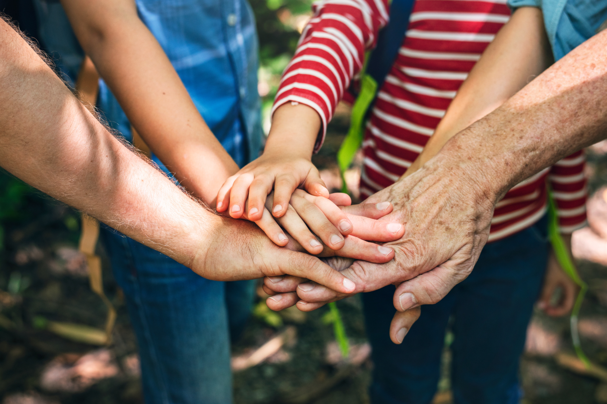 People of different ages stand in a circle and are putting their hands in the middle of the circle.