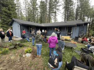 A group of people gathered around a house in a forested area