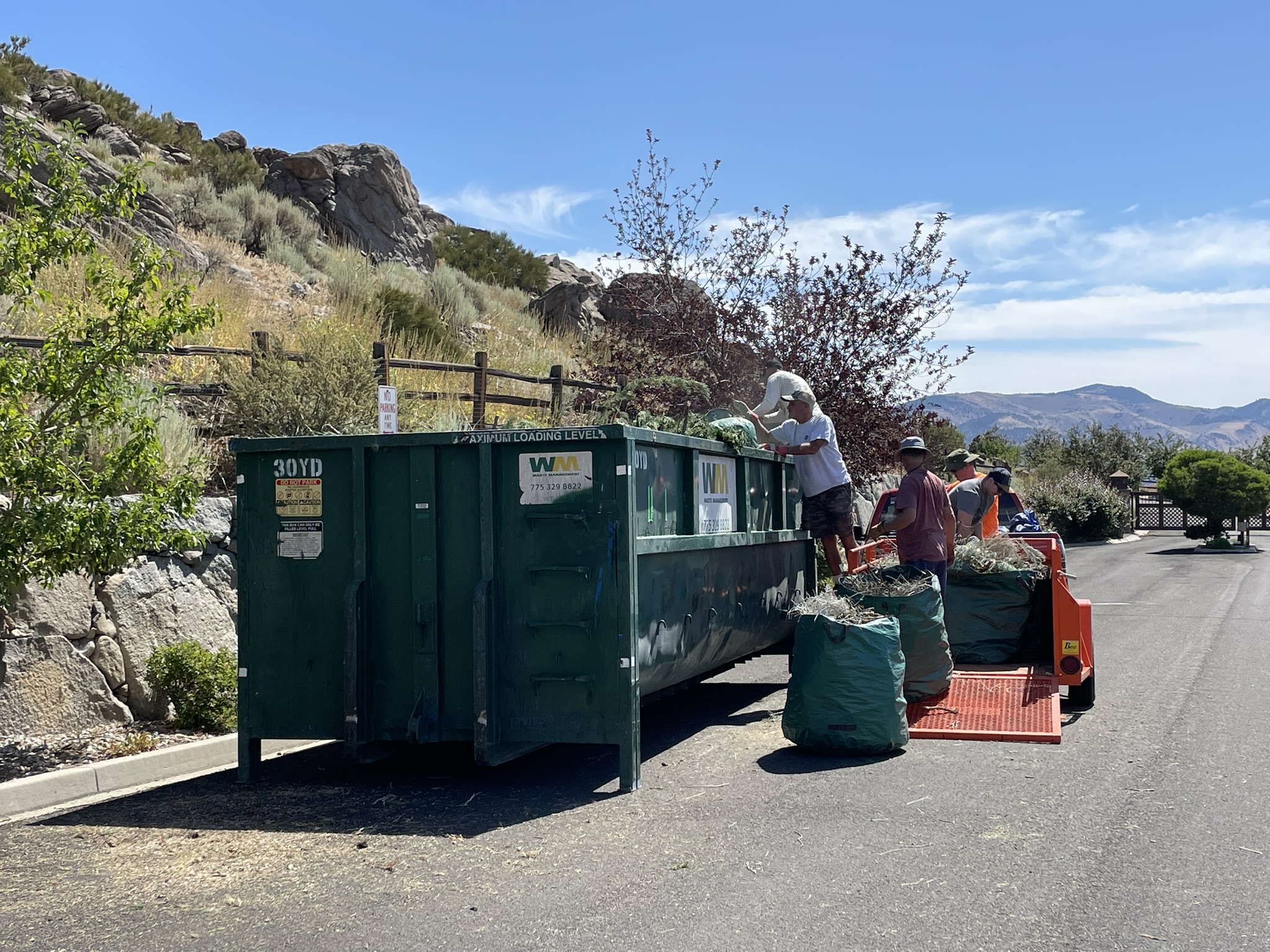 A group of people working together to load bags of green waste into a dumpster